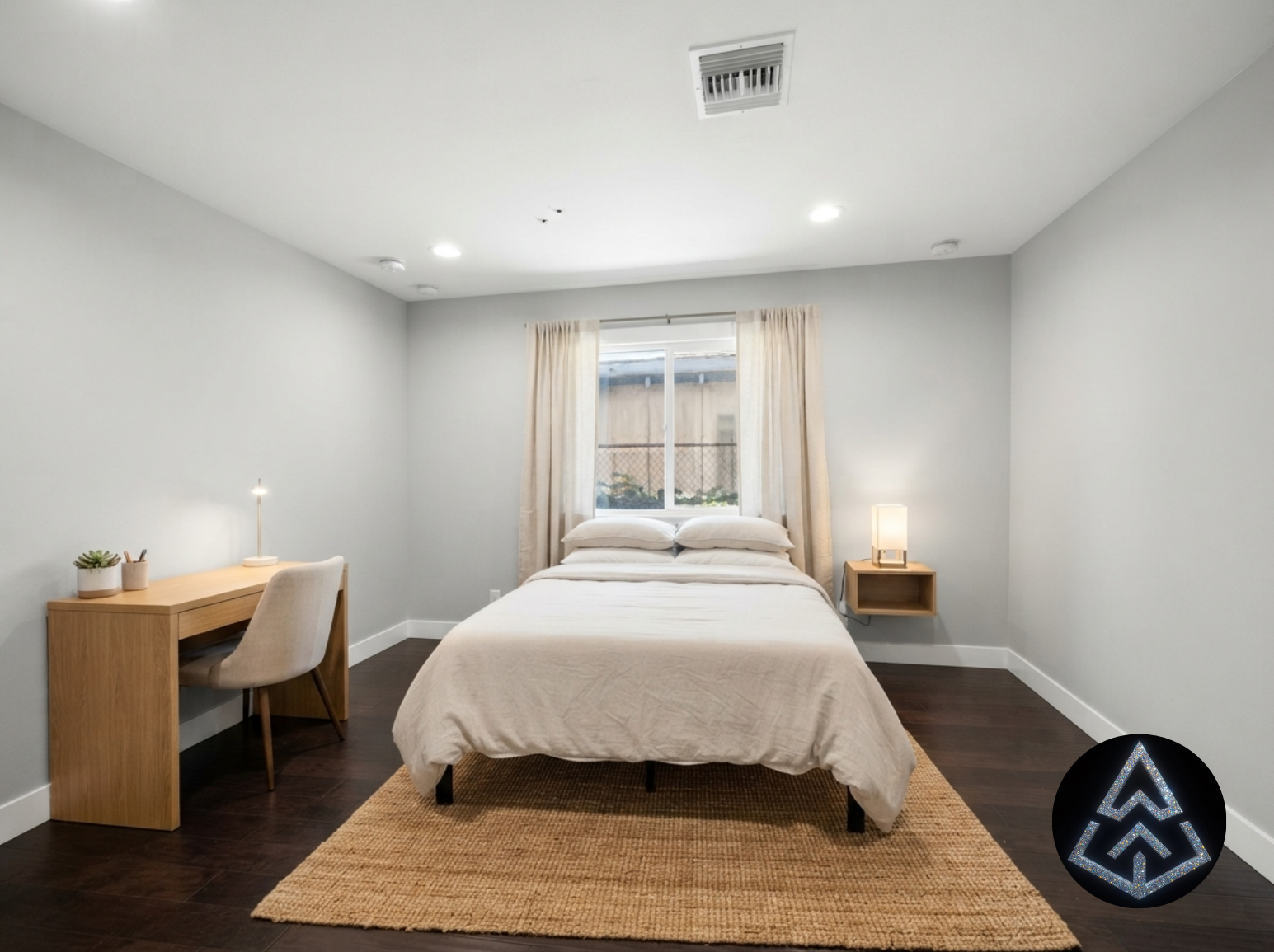Bright furnished bedroom with a queen bed, wood desk and chair, floating nightstand, and a curtained window